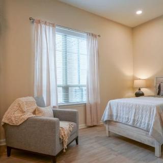 A cozy bedroom with a comfortable bed, armchair, and natural light filtering through the window.