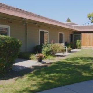 A single-story house with a well-maintained yard and garden under a clear sky.