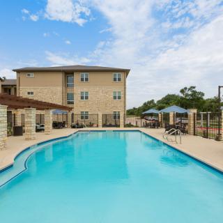 A clear blue swimming pool adjacent to a modern apartment building under a bright sky.