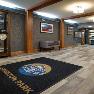 A modern lobby area with stylish decor, featuring a floor mat with the name 'Lexington Park', comfortable seating, and framed artwork on the walls.