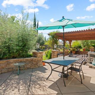 A sunny patio area with outdoor seating and an umbrella, surrounded by lush garden landscaping.