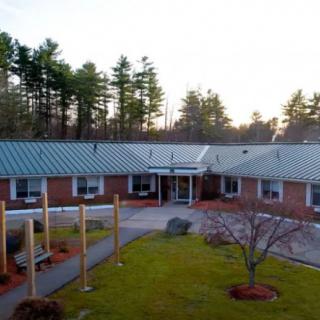 A one-story brick building with a metal roof, surrounded by trees and landscaping at sunset.