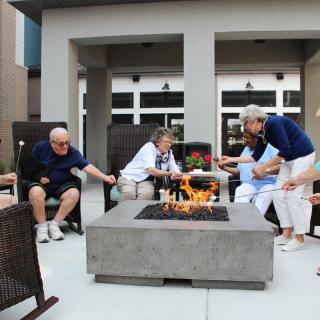 A group of seniors enjoying a relaxing time around a fire pit on a patio.