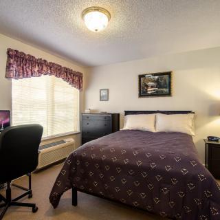 A cozy bedroom with a bed, desk, chair, and window adorned with curtains.