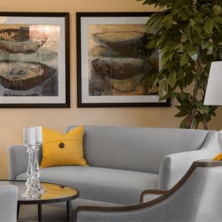 A modern living room with a gray sofa, yellow accent pillow, framed artwork, and decorative elements.