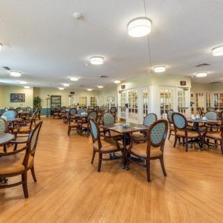 A spacious dining area with wooden floors, multiple tables and chairs, and soft lighting.