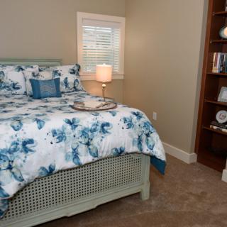 A cozy bedroom with a floral comforter, soft lighting from a bedside lamp, and a bookshelf filled with decor.