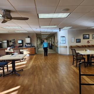 A spacious common area with tables and chairs, leading to a hallway.