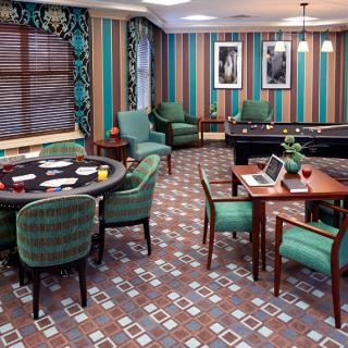 A stylish game room with a poker table and pool table, featuring striped walls, patterned carpet, and comfortable armchairs.