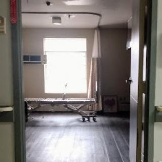 A view into a hospital room with a bed and a window providing natural light.
