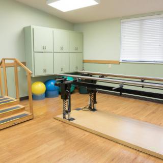 A physical therapy room equipped with balance bars, stairs, and fitness balls for rehabilitation exercises.