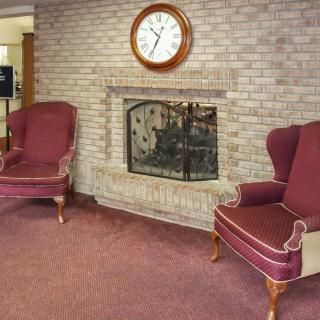A cozy seating area with a brick fireplace, two armchairs, and a clock on the wall.
