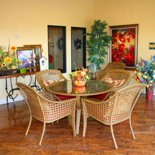 A cozy dining area with wicker furniture, surrounded by vibrant floral arrangements and artwork.