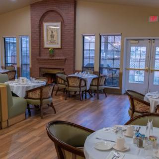 An elegant dining area with tables and chairs set for a meal, featuring large windows and warm lighting.