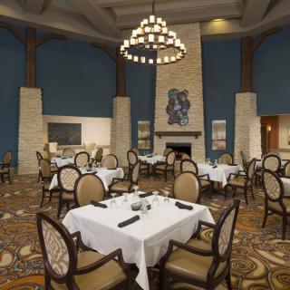 An elegant restaurant interior featuring neatly arranged dining tables, classic chairs, a central chandelier, and a cozy fireplace.
