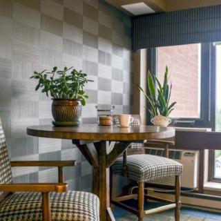 A cozy corner with a small round table adorned with potted plants, flanked by two upholstered chairs near a large window.