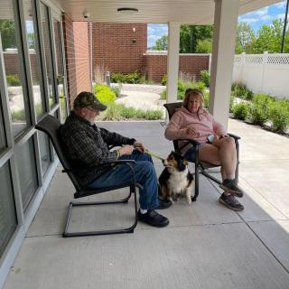 Two people sitting on a patio with a dog between them.