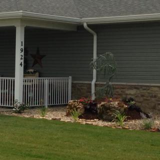 A house exterior with a front porch, landscaped garden, and well-maintained lawn.
