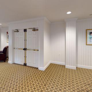 A well-lit hallway featuring double doors, patterned carpet, and framed artwork on the wall.