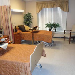 A cozy hospital patient room equipped with two beds, a sitting area, and decorative plants.