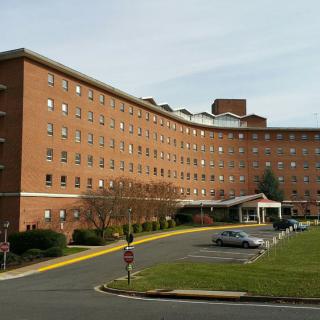 A brick hospital building with a parking area in front.