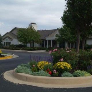A well-maintained building with vibrant landscaping featuring colorful flowers and trees on a cloudy day.
