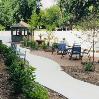 A beautifully landscaped garden with a winding pathway leading to a gazebo, featuring outdoor seating and a fountain surrounded by lush greenery.