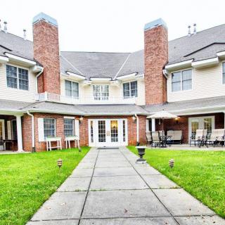 A view of a two-story residential house featuring a well-maintained lawn and patio area.