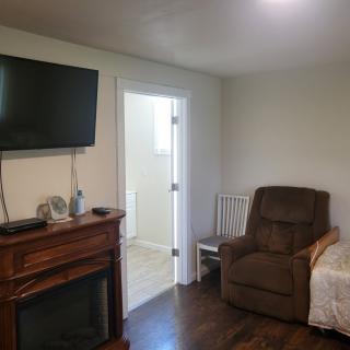 A cozy living room with a TV mounted above a fireplace, a recliner and chair near a doorway.