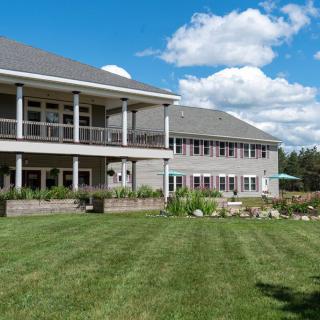 A large house with a spacious lawn under a bright blue sky with scattered clouds.