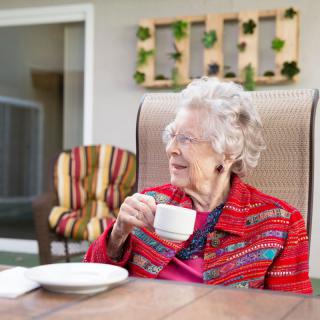 An elderly woman enjoying a cup of tea while sitting outdoors.