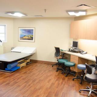 A clean and organized medical examination room with a bed, desk, and computer setup.