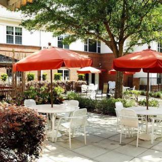 A charming outdoor patio with tables and chairs under bright red umbrellas, surrounded by lush greenery.