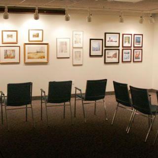 A quiet art gallery room with paintings on the wall and chairs arranged for visitors.