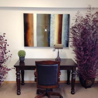 A modern office setup with a wooden desk, chair, and abstract artwork on the wall, complemented by decorative plants.