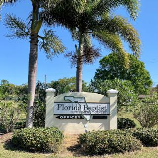 A welcoming sign for Florida Baptist, surrounded by lush greenery and palm trees under a clear blue sky.