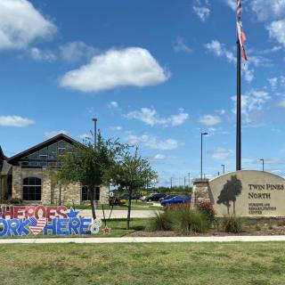 Exterior view of a library with a sign, American flag, and colorful decoration under a blue sky.