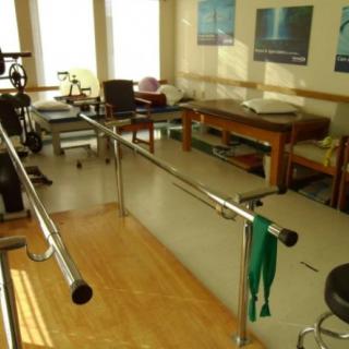 A physical therapy room with parallel bars and treatment tables for rehabilitation exercises.