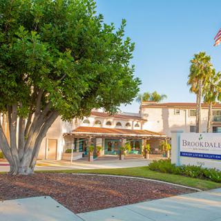 A building with a prominent tree in front and a sign at the entrance, surrounded by palm trees on a clear day.