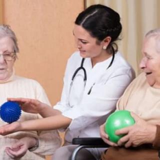 A healthcare professional assists elderly individuals with an exercise activity using colored balls in a nursing home setting.