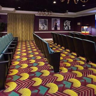 A vibrant and stylish theater room with colorful carpeting and rows of empty seats, adorned with classic movie posters on the walls.