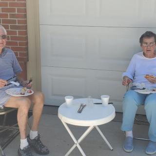Two seniors enjoying a meal outdoors at a small table.