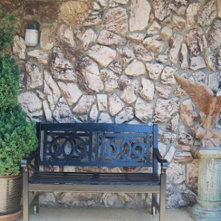 A black metal bench against a textured stone wall, complemented by decorative potted plants.
