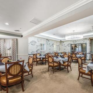 An elegantly designed dining room featuring classic wooden chairs, neatly arranged tables, and a central chandelier.