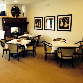 A cozy dining area with neatly set tables and a fireplace, featuring artwork on the walls.