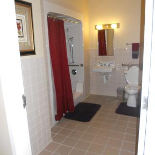 A clean bathroom featuring a shower with a red curtain, toilet, sink, and mirror.