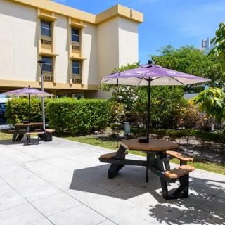 A sunny outdoor patio area with tables, umbrellas, and benches near a building.