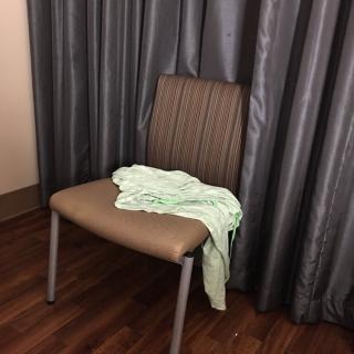 A chair with a piece of clothing draped over it, set against curtains and a wooden floor.