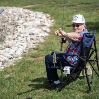 An elderly man enjoys a peaceful day of fishing by sitting comfortably on a chair, casting his line into the water.