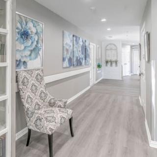 A modern, bright hallway featuring elegant artwork and a patterned chair against light-colored floors.